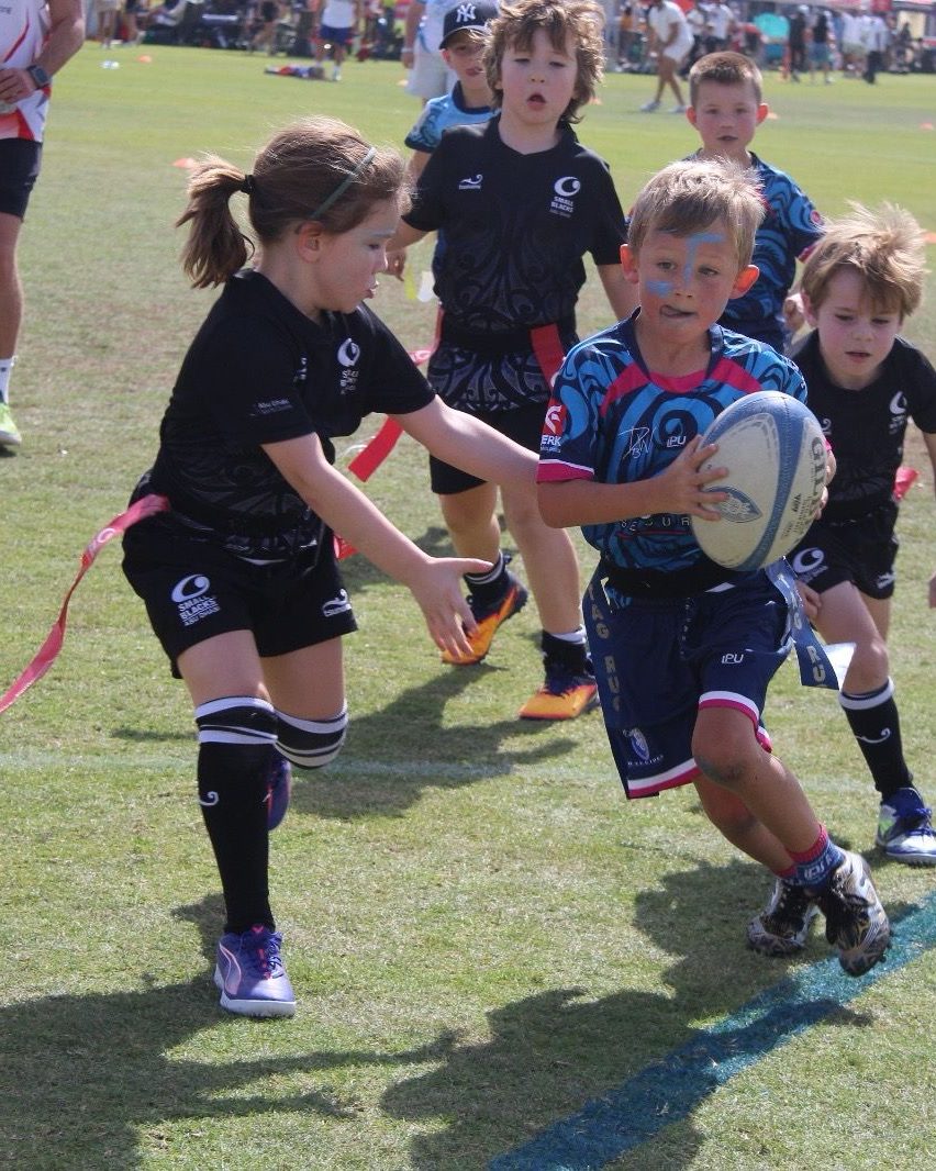 Junior Dubai Warriors player carries the ball past a defender in tag rugby